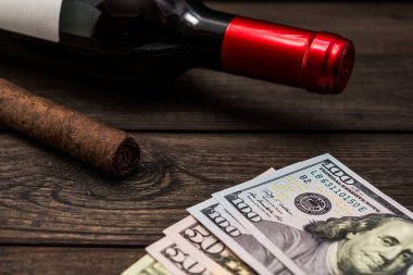Bottle of red wine and cuban cigar with money on an old wooden table