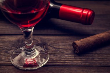 Bottle of red wine with a glass of red wine and cuban cigar on an old wooden table 