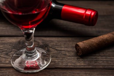 Bottle of red wine with a glass of red wine and cuban cigar on an old wooden table 