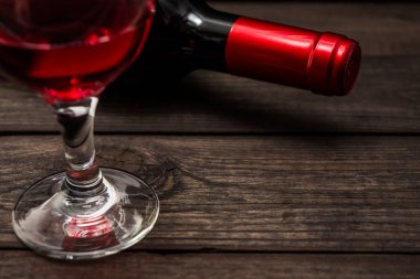 Bir şişe kırmızı şarap ve eski ahşap bir masada bir bardak kırmızı şarap.