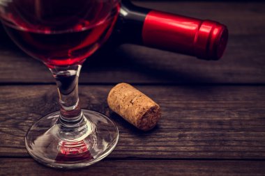 Bir şişe kırmızı şarap ve eski bir ahşap masanın üzerinde bir bardak kırmızı şarap.