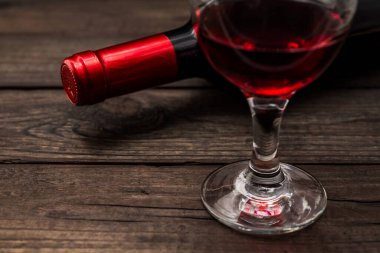 Bir şişe kırmızı şarap ve eski ahşap bir masada bir bardak kırmızı şarap.