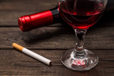 Bottle of red wine with a glass of red wine and cigarette on an old wooden table 