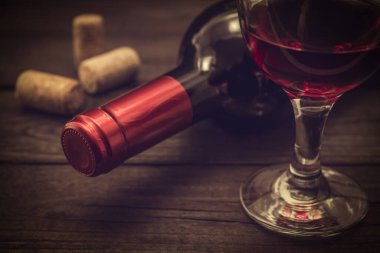 Bottle of red wine with a glass of red wine and corks on an old wooden table 