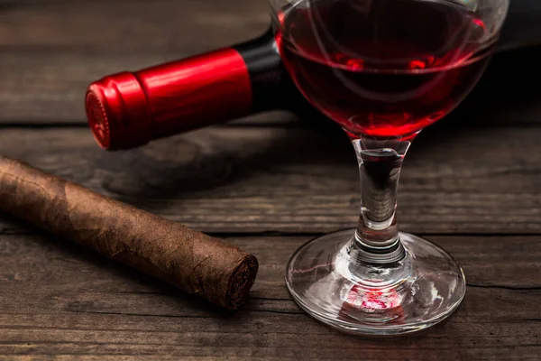 Bottle of red wine with a glass of red wine and cuban cigar on an old wooden table 