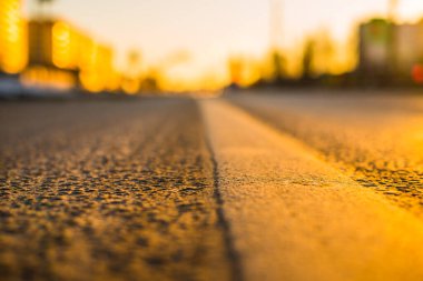 Şehirde güneşli bir gün, asfalt batan güneşin ışınlarıyla aydınlanıyor..