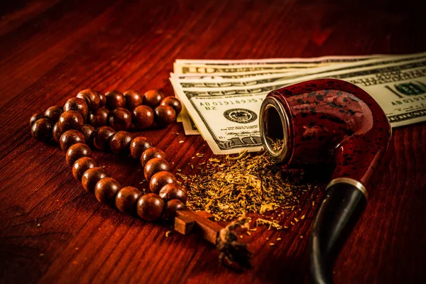 Tube for smoking tobacco with money and rosary with a cross on a