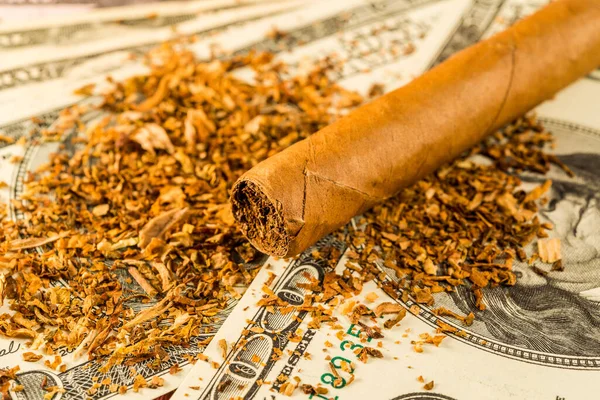 Cuban cigar and tobacco leaves lie scattered on the dollar bills