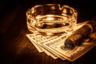 Küba purosu, üzerinde cam kül tablası ve birkaç dolarlık banknotlar var. 