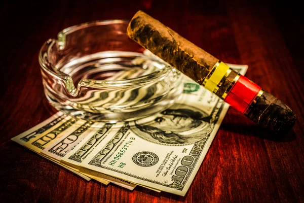 Cuban cigar with glass ashtray on a several dollar bills on the