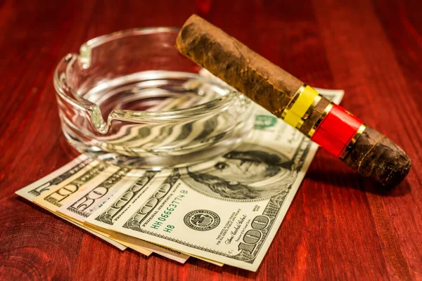 Cuban cigar with glass ashtray on a several dollar bills on the