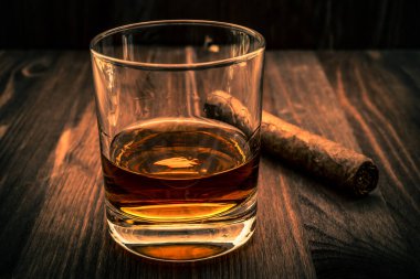 Tahta bir masada bir bardak viski ve Küba purosu. Odaklan.