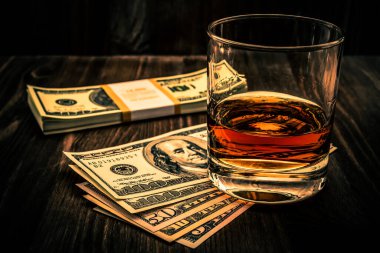 Tahta bir masanın üzerinde bir paket dolarla bir bardak viski. V açısı