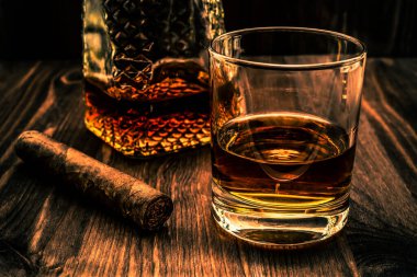 Bir bardak viski ve Küba purosuyla ahşap bir tabakta.