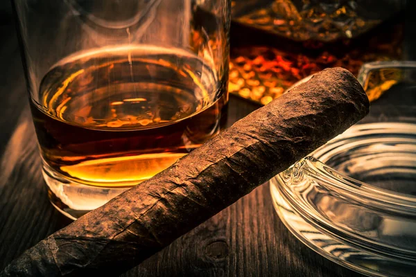 Bir bardak viski ve Küba purosuyla ahşap bir tabakta.
