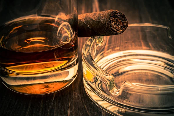 Glass of whiskey and cuban cigar with ashtray on a wooden table