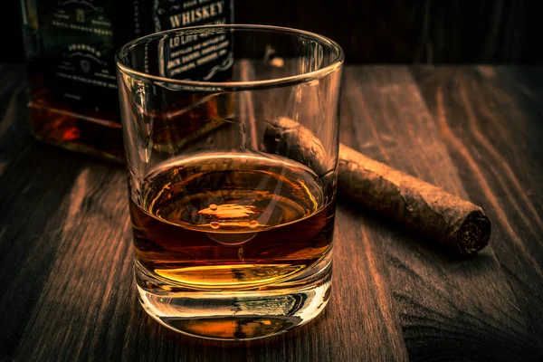 Bir şişe viski ve bir bardak Küba purosu ahşap bir masada.