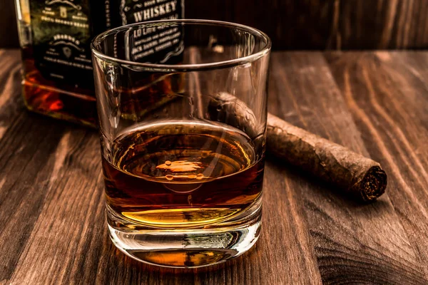 Bir şişe viski ve bir bardak Küba purosu ahşap bir masada.