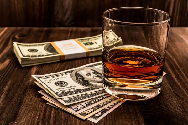 Tahta bir masanın üzerinde bir paket dolarla bir bardak viski. V açısı