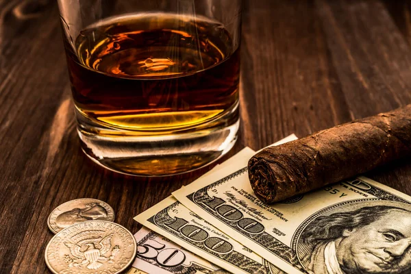 Glass of whiskey and a money with cuban cigar on a wooden table.