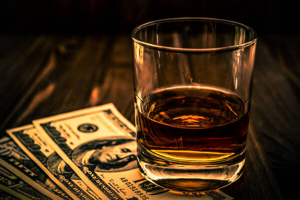 Glass of whiskey and revolver with a money and tobacco pipe on table
