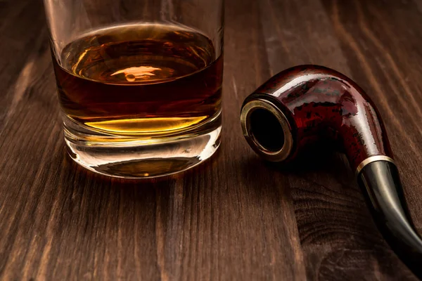 Glass of whiskey and tobacco pipe on a wooden table