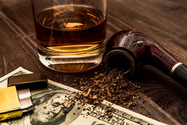 Glass of whiskey with a money and tobacco pipe with tobacco leav