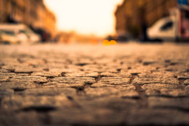 Şehir meydanı taşla döşenmiş, güneş ışığı asfalta düşüyor.