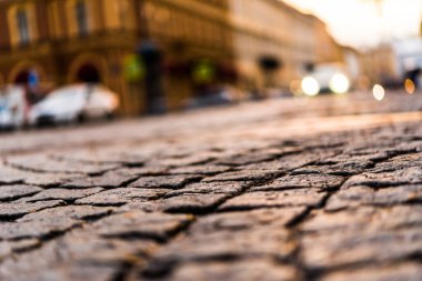 Şehir caddesi taşla kaplı, yaklaşan ışıklarla parlıyor. 
