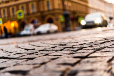 Şehir caddesi taşla kaplı, yaklaşan ışıklarla parlıyor. 