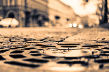 Şehir meydanı taşlarla döşenmiş, arabalar yolda.