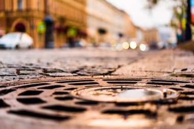 Şehir meydanı taşlarla döşenmiş, arabalar yolda.