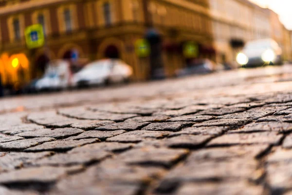 Şehir caddesi taşla kaplı, yaklaşan ışıklarla parlıyor. 