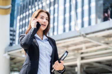 Asyalı genç ve zeki iş kadını şehirde telefonla konuşuyor. Elinde kahve fincanı olan kız gülen yüzle işe gidiyor. İş konsepti için telekomünikasyon ve mobil ağ.