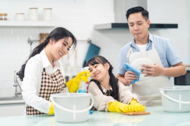 Asyalı genç bir aile kızlarına mutfak tezgahını temizlemeyi öğretiyor. Çocuk ve ailesi birlikte dans edip, eğlenerek gülümsüyorlar. Evi mutlulukla temizlerken mutlu bir aile anı..