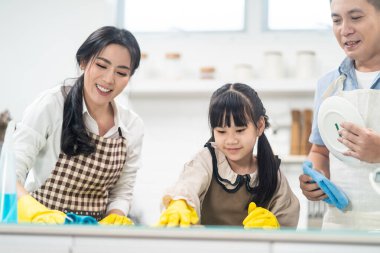 Asyalı genç bir aile kızlarına mutfak tezgahını temizlemeyi öğretiyor. Çocuk ve ailesi birlikte dans edip, eğlenerek gülümsüyorlar. Evi mutlulukla temizlerken mutlu bir aile anı..