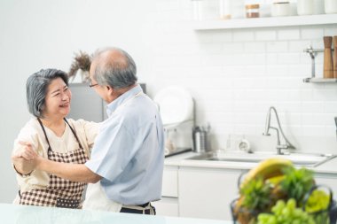 Asyalı mutlu yaşlı çift evde mutfakta duruyor emekliliğin ve birlikte dans etmenin tadını çıkarıyor. Yaşlı dedeleri sevmek gülen yüzle yemek pişirmek. Evde ilişki ve aktivite.