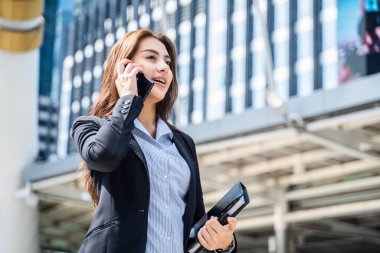 Asyalı genç ve zeki iş kadını şehirde telefonla konuşuyor. Elinde kahve fincanı olan kız gülen yüzle işe gidiyor. İş konsepti için telekomünikasyon ve mobil ağ.