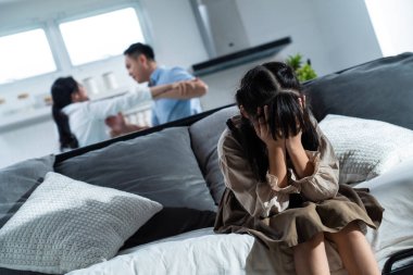 Asyalı kız çocuk evde ebeveynler kavga ederken ya da kavga ederken yatakta oturup ağlıyor. Yüzü ve gözleri ellerle kaplayan çocuk şiddeti görmek istemiyor. Ailede aile içi sorunlar.