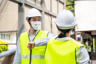 Asyalı işçiler, covid salgınından dolayı mimari alanında koruyucu yüz maskesi takıyorlar. Erkek ve kadın mühendisler, koronavirüs enfeksiyonunu önlemek için el sıkışmak yerine dirsek teması yapıyorlar..