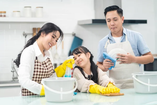 亚洲的年轻家庭教女儿打扫厨房柜台 孩子和父母一起跳舞 笑得很开心 当幸福地打扫房子时 温馨家庭的快乐时刻 — 图库照片