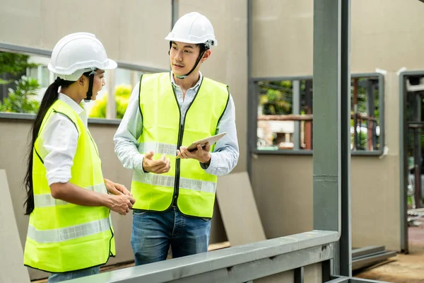 Asian Colleagues worker Specialists team wearing protective safety hard hat helmet use tablet on Construction Site. Civil Engineer and architecture discuss about Real Estate Building Project work plan