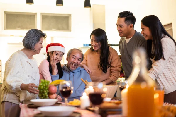 Happy family time and relationship, Asian big family having small Christmas party eating food together at home. Kid is happy to see parent, cousin preparing food and bring it to dining table at home.