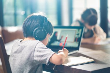 Asyalı küçük çocuklar evde kendi kendilerine öğreniyorlar. Evde e-öğrenim için tablet ve kulaklık kullanan çocuk. Kağıt çarşafa ödev notu yazan kız. Eğitim ve teknoloji kavramı