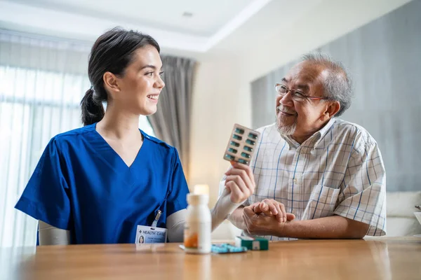Asian Senior male patient consult with physician nurse at nursing home. Caregiver therapist pharmacist girl hold medicine pills bottle, explain prescription to elderly older disabled guy in house care