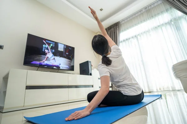 Asyalı güzel genç kadın evde kalıp, online eğitmenin talimatlarını takip ediyor. Ev Yogası 'nda kilit altında tutulan aktif kız Coronavirus salgını sırasında pilates egzersizi yapıyor..