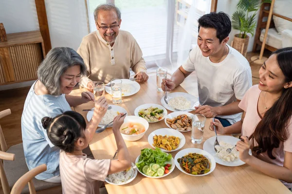 Asyalı mutlu aile yemek masasında öğle yemeği yiyor. Küçük kız, baba, anne ve büyükbaba ile birlikte yemek yemekten hoşlanıyor. Evde çok nesilli ilişki ve aktivite