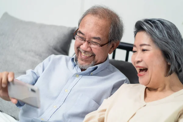 Asian old woman and old man hold mobile phone or tablet for talking and smiling on video call with nephew for remote party during COVID at home. Grandparents feel happy with communicate via internet.