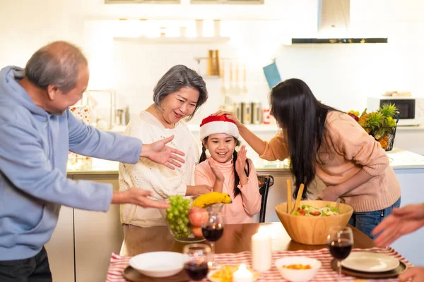 Happy family time and relationship, Asian big family having small Christmas party eating food together at home. Kid is happy to see parent, cousin preparing food and bring it to dining table at home.