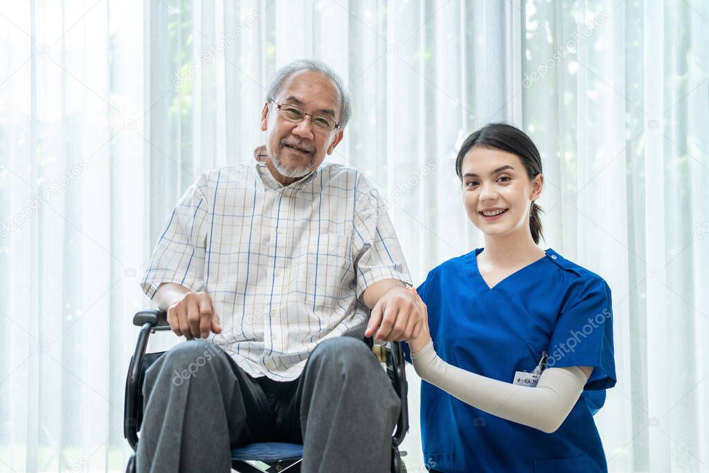 Portrait of Happy Asian disabled Senior Elderly male on wheelchair enjoy stay home nursing care. Beautiful nurse caregiver woman sit beside older patient, looking at camera. medical insurance concept.